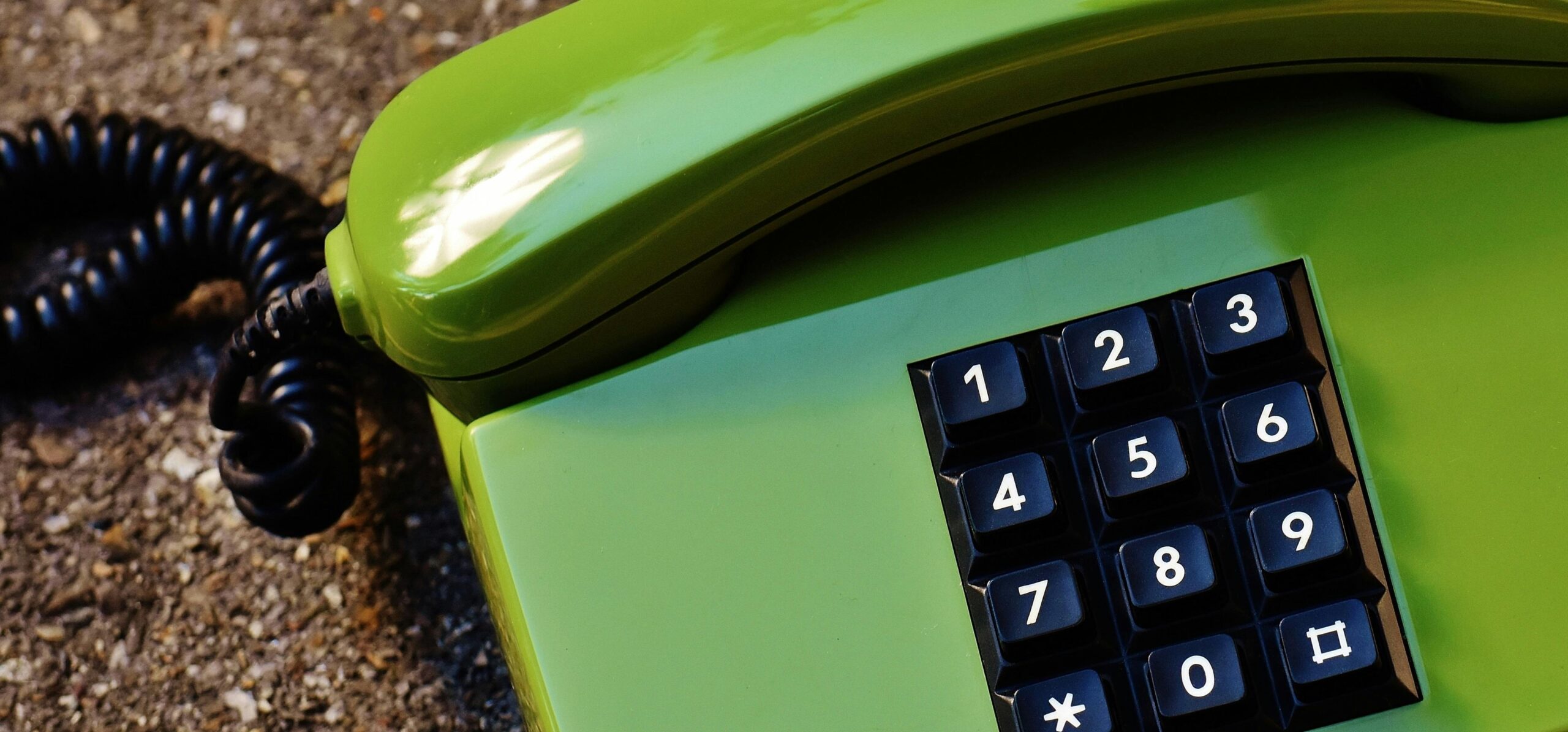 Close-up of a retro green telephone with rotary dial and numeric keypad on a textured surface.
